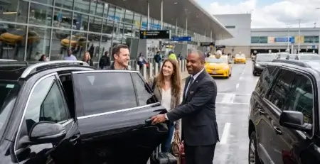 Motorista brasileiro Newark Airport abre a porta de um SUV preto para um casal com malas na frente do terminal